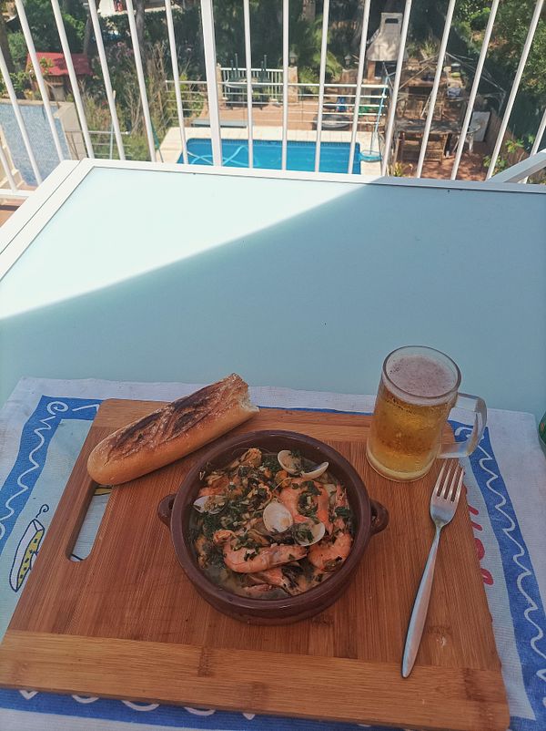 A cozy outdoor dining setup featuring a delicious seafood dish, bread, and a beer.
