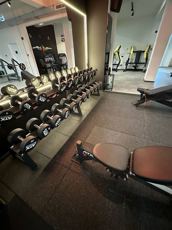 The image captures a well-equipped gym area featuring a rack of dumbbells and a workout bench.