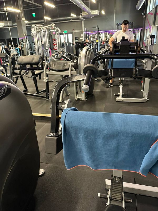 A gym interior featuring various workout equipment and a person preparing to exercise.