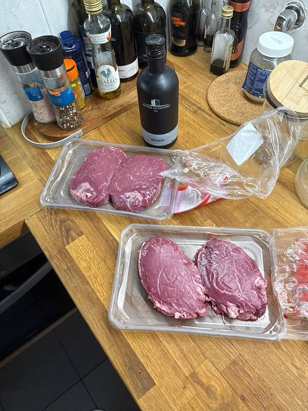 The image features several cuts of steak on a kitchen countertop alongside various condiments and bottles.