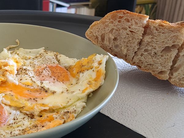 A bowl of fried eggs is presented alongside a slice of sourdough bread.