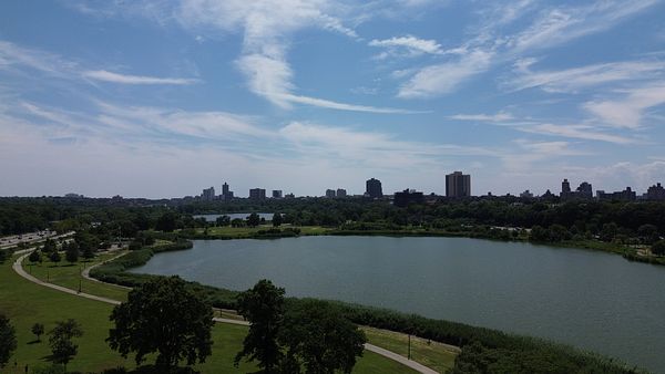 A small drone flying outdoors with a cloudy sky and trees in the background.