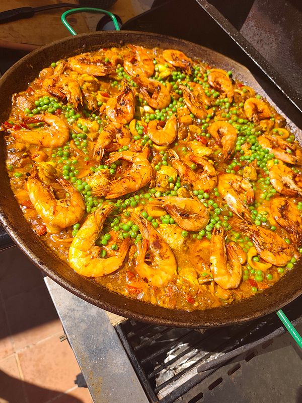 Morning beach scene with a wooden table featuring homemade paella and breakfast items overlooking the ocean.