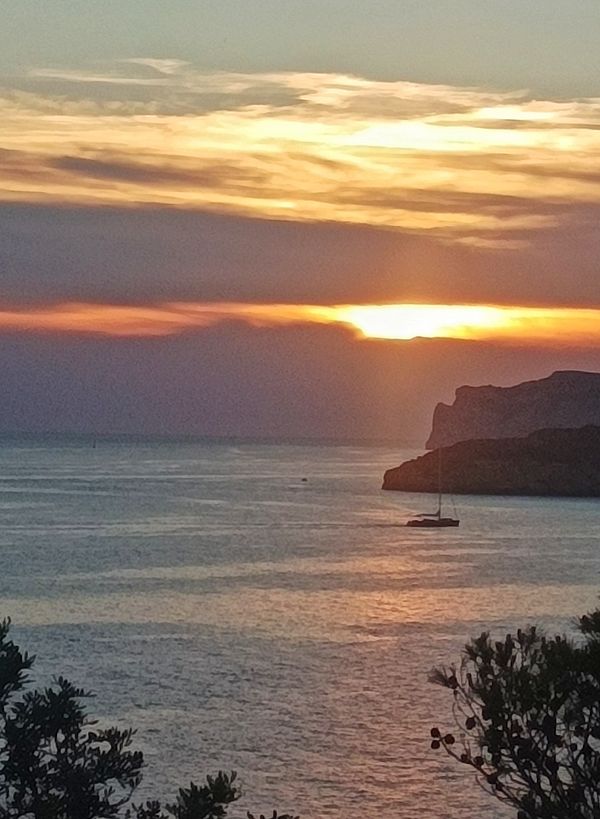 A picturesque sunset over the ocean with a sailboat in the foreground.