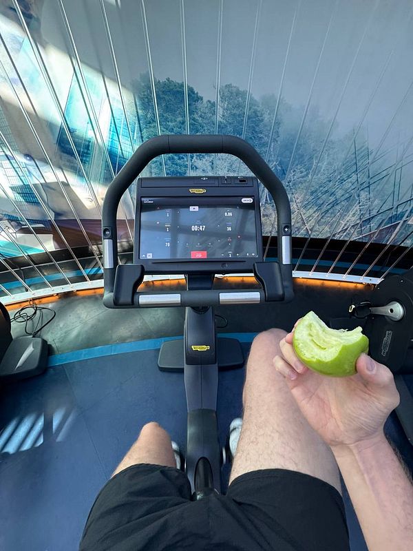 A person is exercising on a stationary bike while holding a piece of green apple.