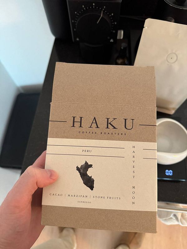 A person holds a coffee bean package from Haku Coffee Roasters, featuring details about the beans and their origin.