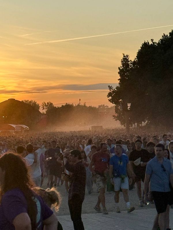 A large crowd of festival-goers is seen walking towards the camera during sunset, with a hazy atmosphere.