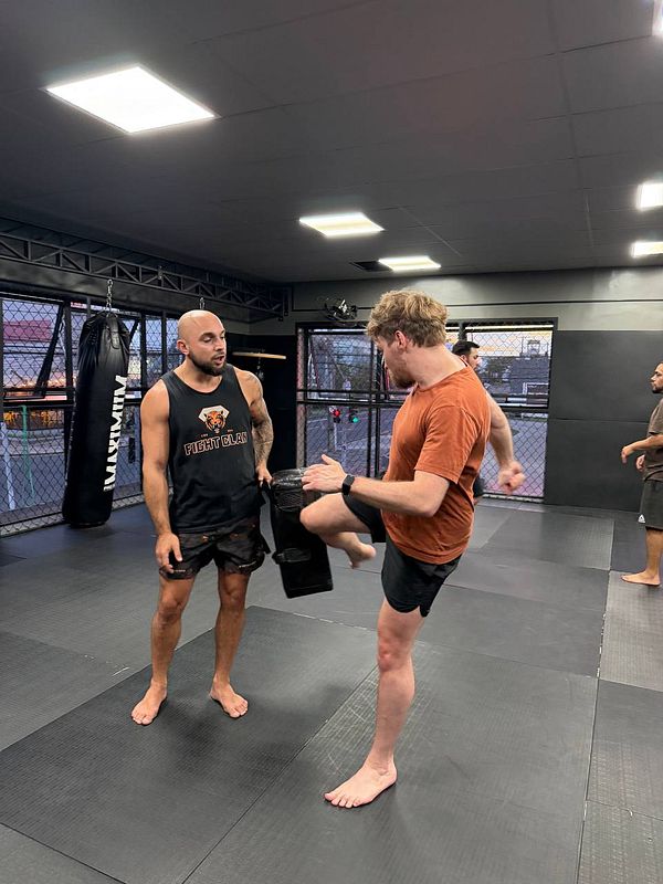 A man wearing boxing gloves practices Muay Thai with a female trainer in a gym setting.