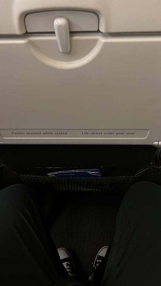 The image captures a view from an airplane seat, focusing on the seat pocket and safety instructions.
