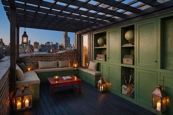 A dark academia-inspired rooftop patio features olive green built-in cabinets and benches, a dark wood pergola overhead, and a low brick parapet framing a city skyline at dusk. Lanterns with candlelight, patterned cushions, and a small wood coffee table create a warm, scholarly atmosphere.