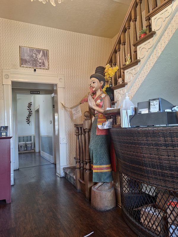 The image captures the interior of a Thai restaurant featuring a decorative statue and a reception area.