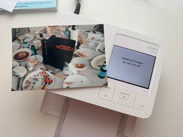 Photo printer with a printed photo showing a cat, placed on a wooden table with various objects in the background.
