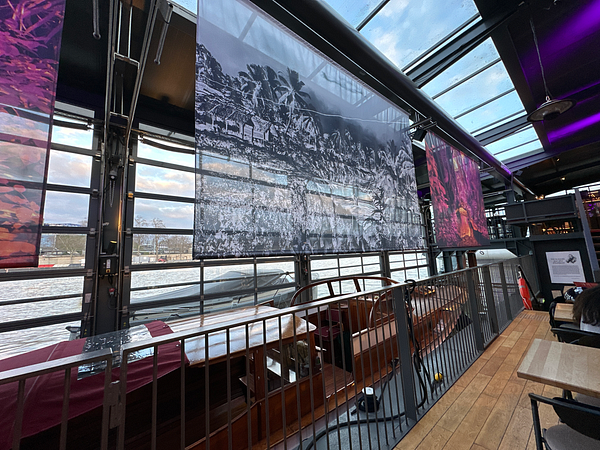 The image captures an interior view of a modern space with large photographic displays and a scenic waterfront.
