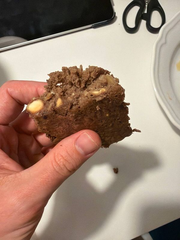 A stack of brownie banana pancakes drizzled with chocolate sauce and topped with sliced bananas and blueberries, served on a white plate.