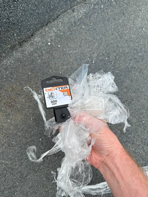 A hand holds a plastic-wrapped tool on a textured roof surface.