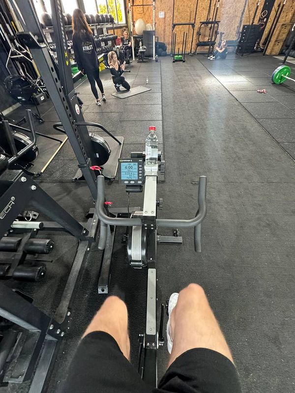 A view from a rowing machine in a gym setting, showing workout activity and equipment.
