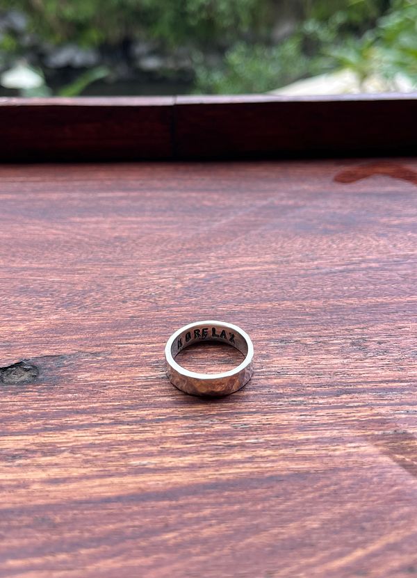 A handmade silver ring is displayed on a wooden surface.