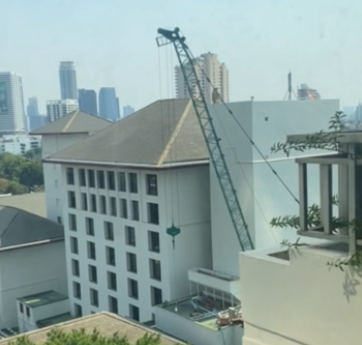 A construction crane is lifting a green object near a building in an urban setting.