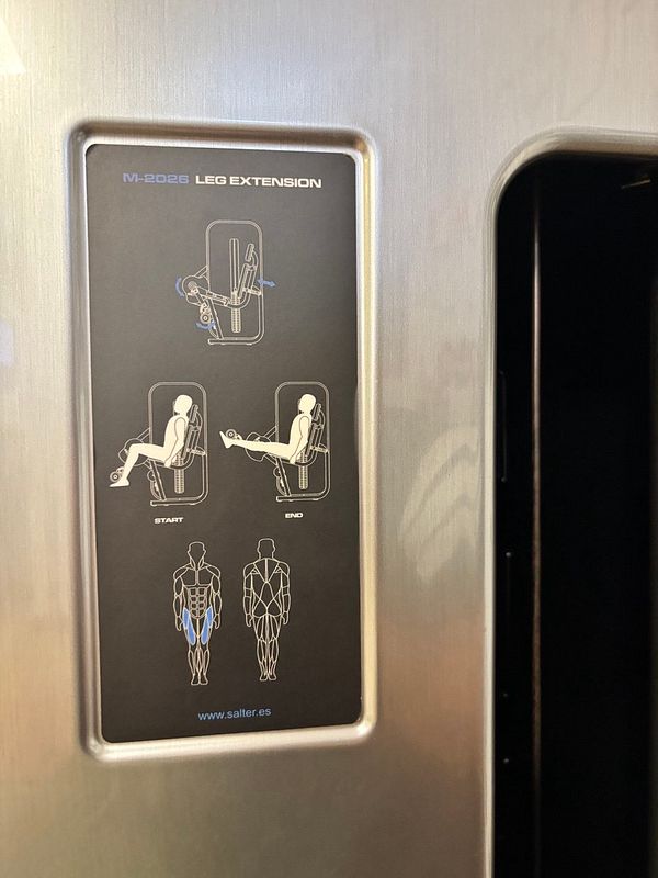 The image displays an instructional panel for a leg extension machine at a gym.