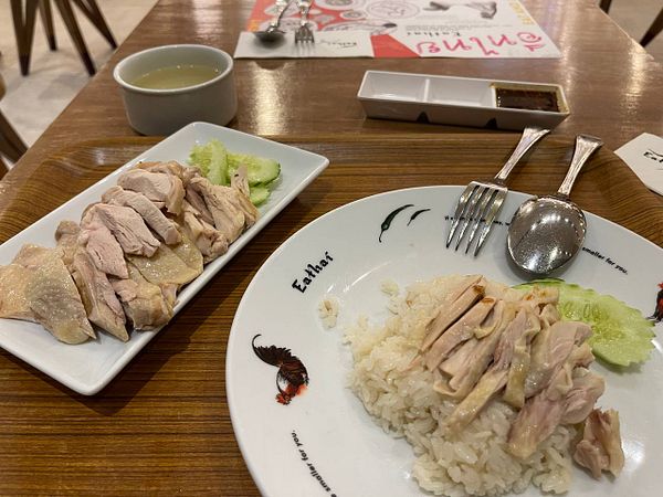 A plate of chicken rice served with sliced chicken, cucumber, and a bowl of soup.