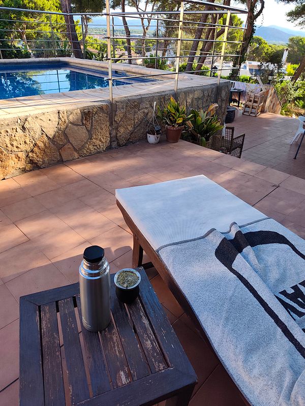 A serene early morning poolside setting with a traditional mate cup and a phone on a white wooden table.