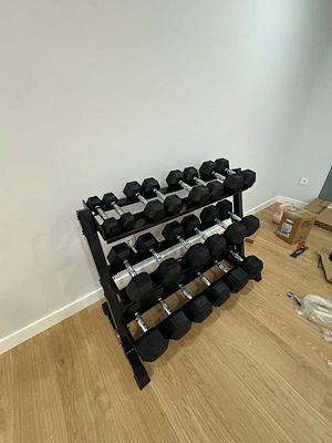 A compact dumbbell rack filled with various weights is positioned against a plain wall.