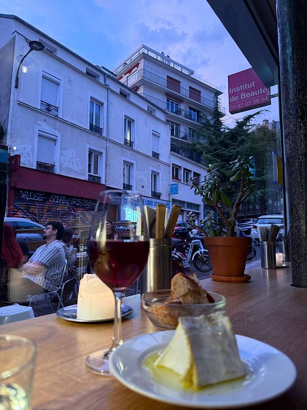 A cozy café scene featuring a glass of red wine, dessert, and a view of the street outside.