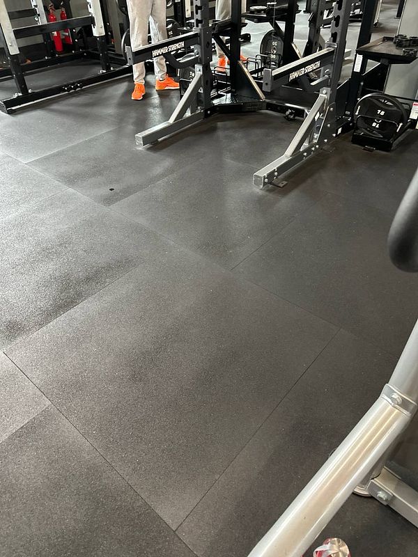 The image captures a section of a gym floor with workout equipment and a person in the background.