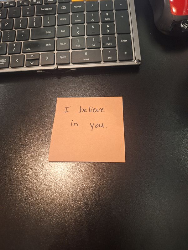 A handwritten note on a sticky pad conveys a message of encouragement.