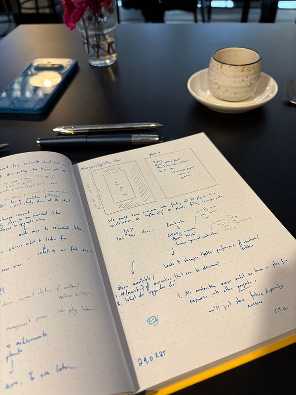 A workspace featuring a notebook with design sketches and notes, a smartphone, a pen, and a coffee cup.