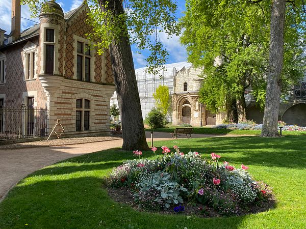 Park promenade featuring a woman and a young girl walking along a paved path flanked by green grass and autumn foliage.