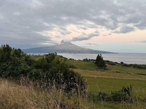 A scenic view of a volcanic mountain overlooking a body of water, surrounded by lush greenery and cloudy skies.