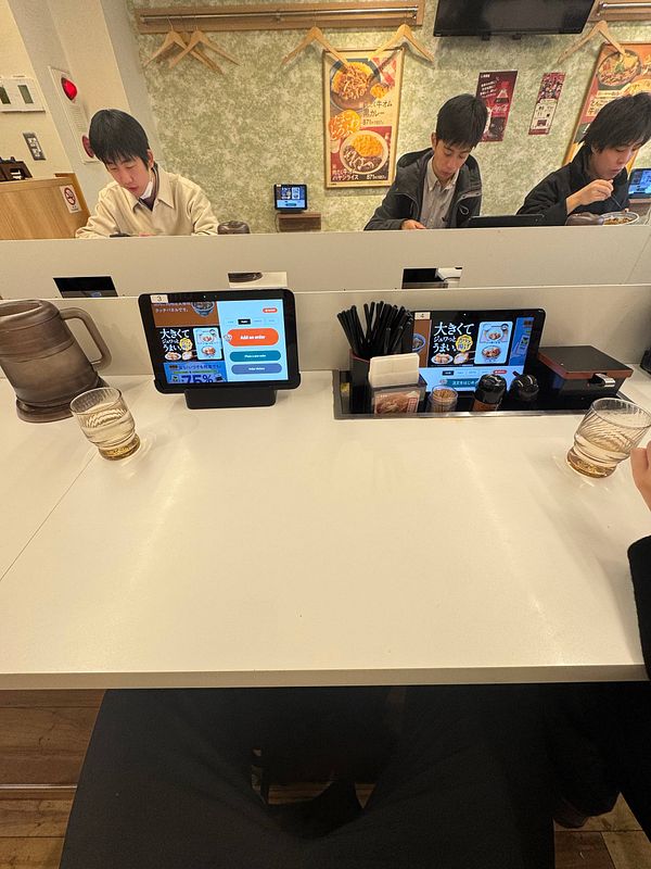A dining scene at Yoshinoya featuring customers and digital ordering tablets.