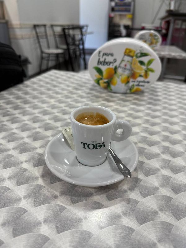 A small cup of coffee is placed on a table in a café setting.