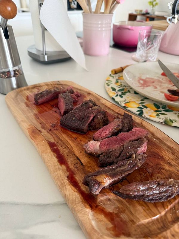 A man grilling several pieces of steak on a Tesla Powerwall unit outdoors during daylight.