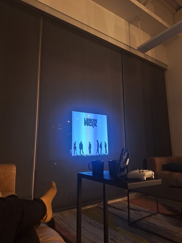 A cozy living room scene featuring a projector displaying a Linkin Park image on a wall.