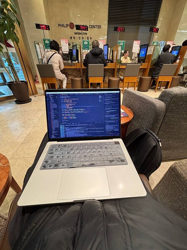 A laptop displaying code is positioned on a person's lap in a medical center lobby.