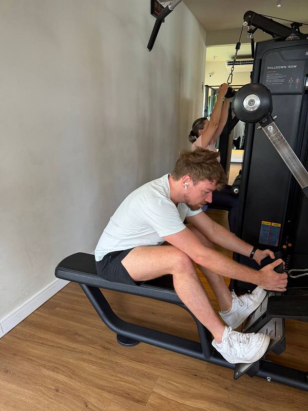 A gym workout scene featuring two men exercising on treadmills in a modern gym setting, with a third person visible in the background near gym equipment.
