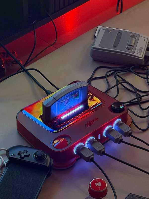 Retro gaming console setup with a plugged-in 'Mario Kart' cartridge and connected controllers on a table with ambient red lighting.
