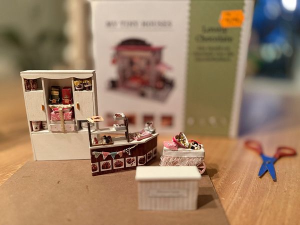A detailed miniature display of a chocolate shop with various sweets and a backdrop box.