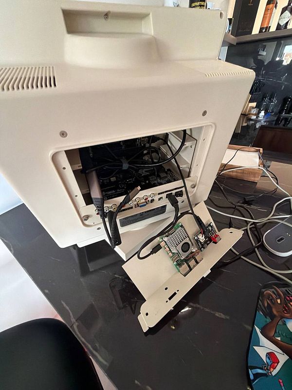 A retro beige computer monitor with its back panel open, showing internal components and a Raspberry Pi 5 connected externally on a lowered panel.