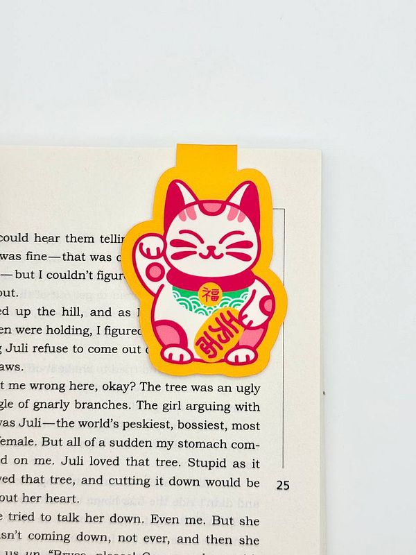 A colorful cat-shaped magnetic bookmark is placed on an open book page.