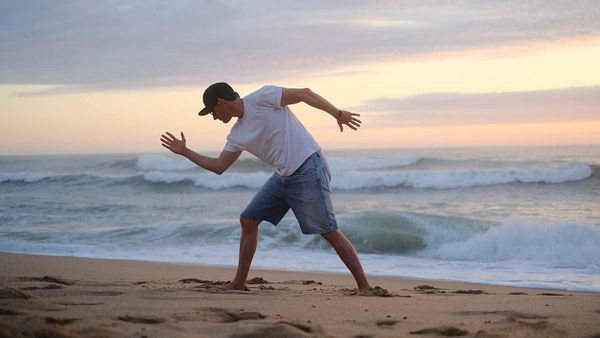 A dancer performs a modern dance pose on a beach at sunset.