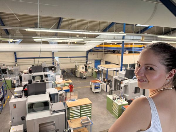 A woman stands in a factory overlooking various machines and workstations.