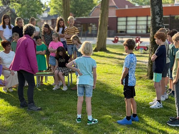 A group of children and adults are gathered outdoors, engaged in a photography session.
