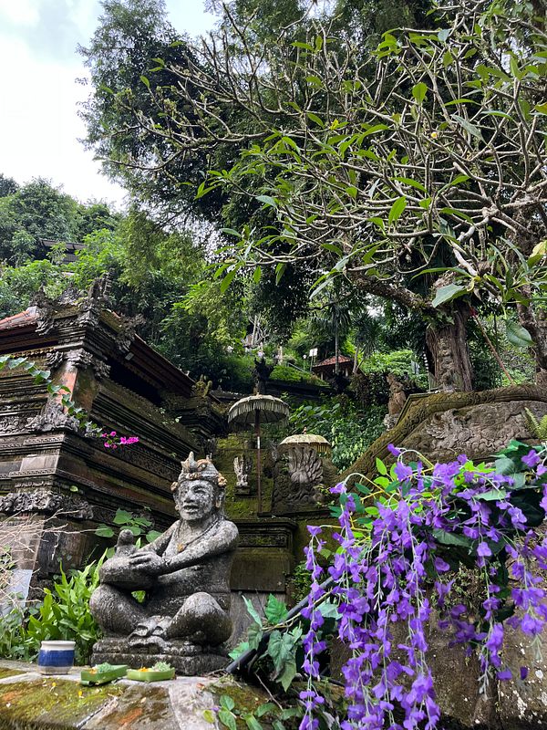A serene Balinese landscape featuring a stone statue, lush greenery, and vibrant flowers.