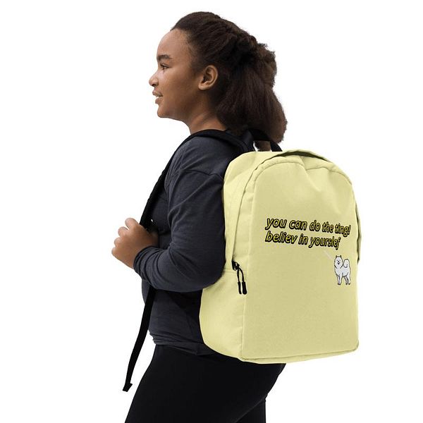 A young girl is wearing a light yellow backpack with motivational text and a cartoon dog design.