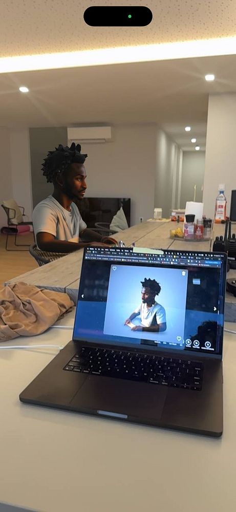 A person is seated at a table with a laptop displaying a 3D model of themselves.