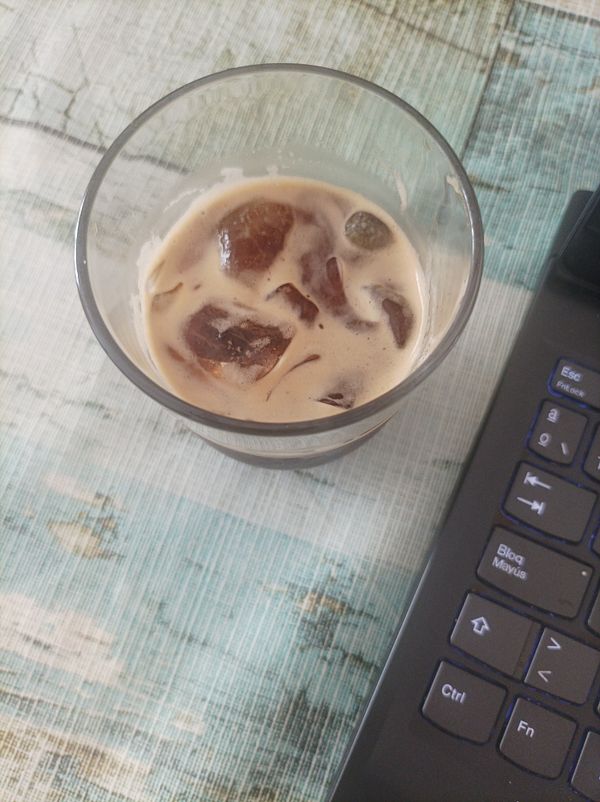 A glass of iced espresso sits next to a laptop on a textured surface.