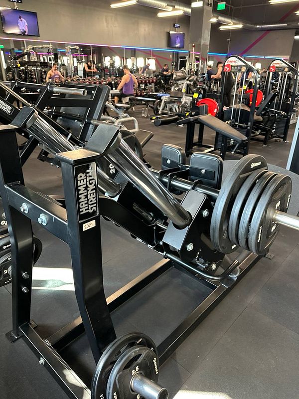 A gym interior featuring a Hammer Strength leg press machine with weights.